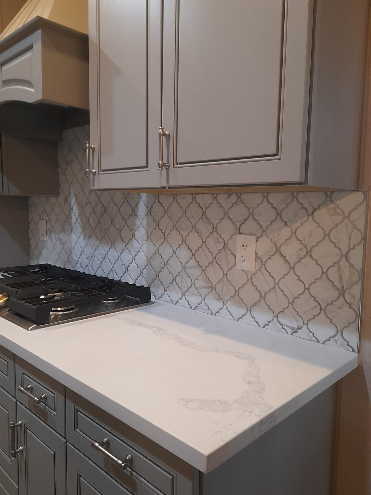 Marble-look arabesque lantern tile backsplash behind a gas cooktop with quartz countertop