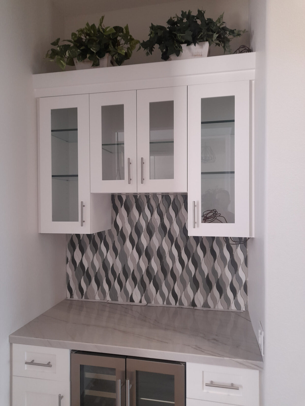 Gray wave-pattern mosaic tile backsplash in a beverage bar with glass-front cabinets